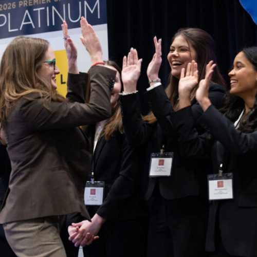 Business students in professional clothes high five with their coach after presenting at a case competition.