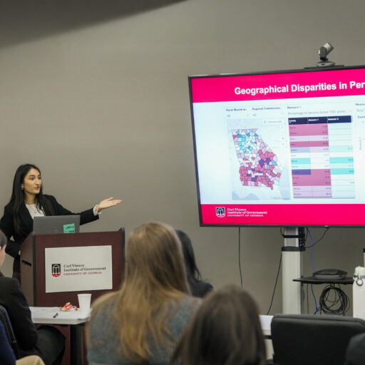 A student presents at a podium with a Carl Vinson Institute for Government sign in front of a heat map of the state of Georgia. 