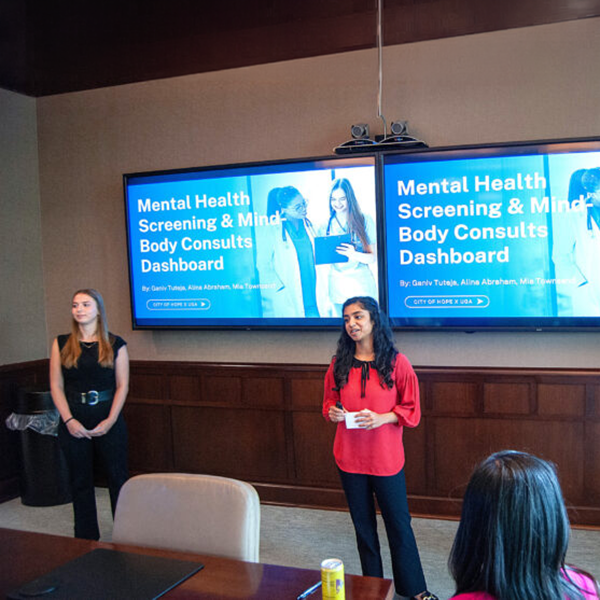 Students present in a boardroom in front a projected slide that reads 