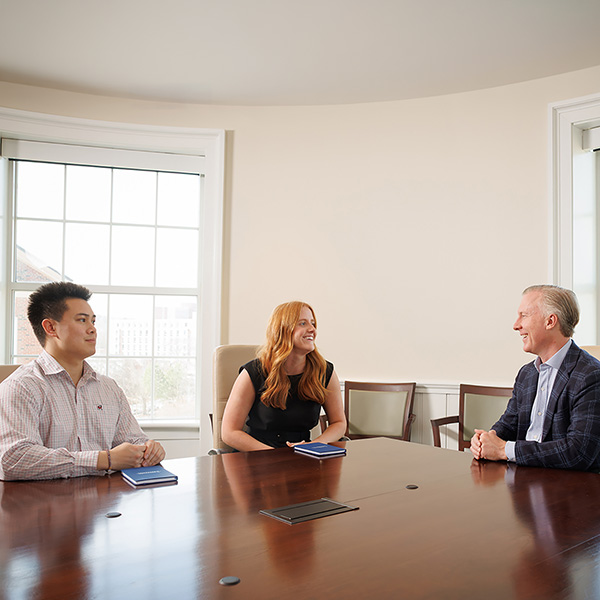 Wes Rogers sits with two Terry College students at a large conference table.