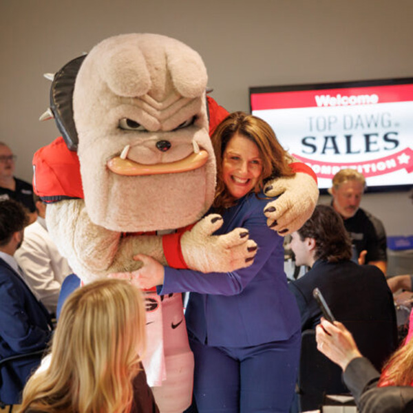 UGA Hairy Dawg shares a side hug Terry College Sales lecturer Cindy Ripe in front of a electronic sign reading 