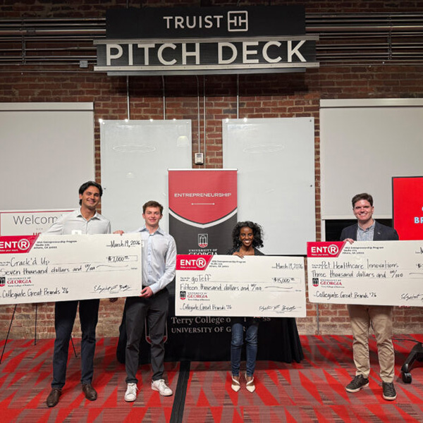 Young entrepreneurs stand below a Truist Pitch Deck Sign at Studio 225 hold novelty large prize checks.