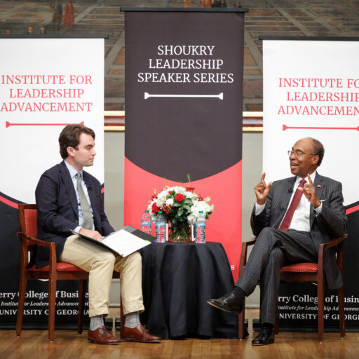 Federal Judge Steve Jones is interviewed by one of his law clerks. They both sit in arm chairs on stage at the UGA Chapel with Institute for Leadership Advancement banners behind them.