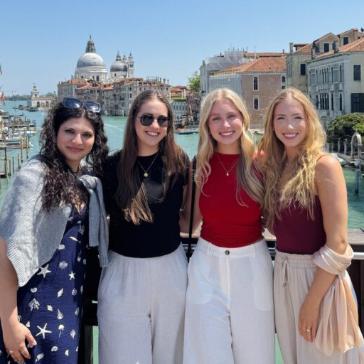 Kelsie Pearson stands with three other young women on a bridge over a European canal with historic buildings stretching behinds them.