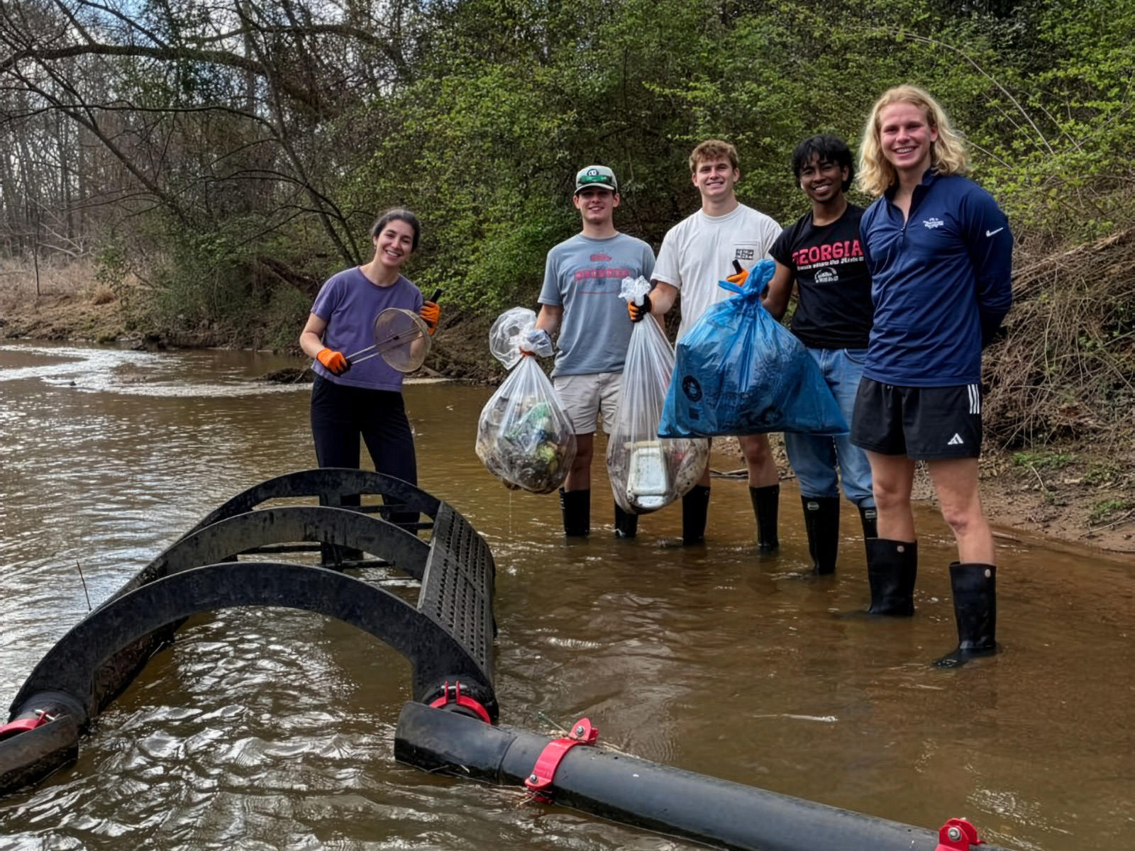 Students stand in stream on the UGA Campus with bags of litter