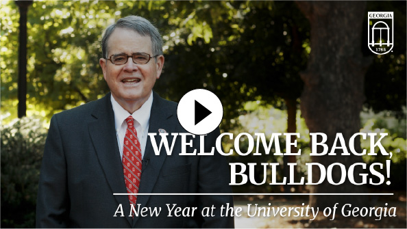 University of Georgia President Jere Morehead stands outdoors in front of trees, smiling alongside large text reading 'WELCOME BACK, BULLDOGS! A New Year at the University of Georgia' and a central white play button icon.