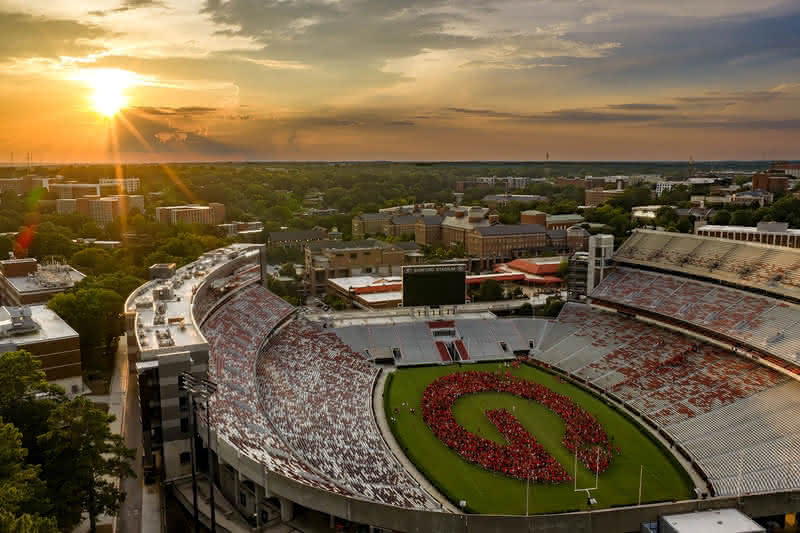 An aerial view at sunset shows students standing together on the football field at Sanford Stadium to form a giant red 'G' logo.
