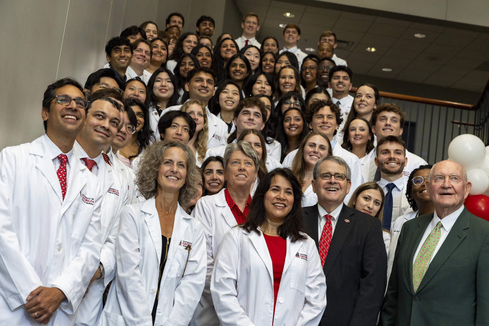 A smiling student receives her white medical coat on stage during a White Coat Ceremony in front of an audience.